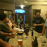 A group of people gathered around a counter drinking homebrew and eating