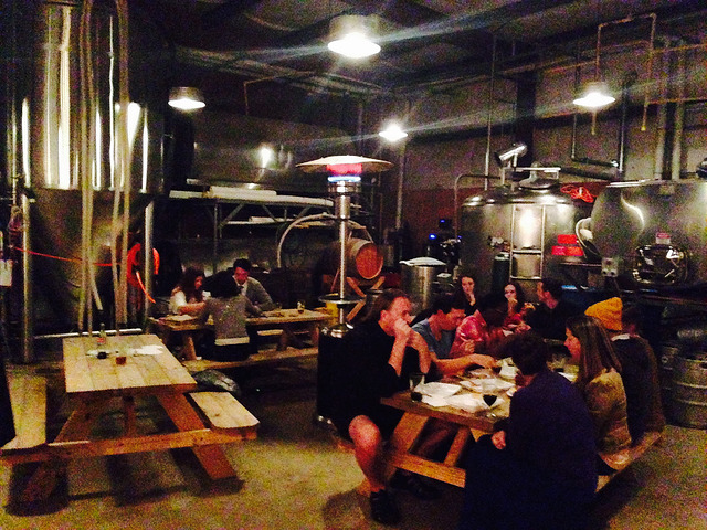 A group of tables with people eating thanksgiving dinner among brewery equipment. 